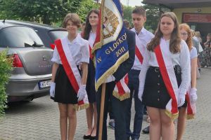 Uczniowie stoją ze sztandarem przed szkołą.