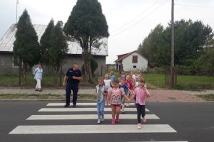 Dzieci wraz z policjantem przechodzą przez jezdnię.