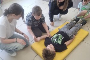 Uczeń klasy pierwszej leży na materacu i czeka na ćwiczenia z pierwszej pomocy.