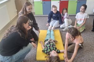 Uczennica klasy pierwszej leżąca na materacu czeka na ćwiczenia z pierwszej pomocy.