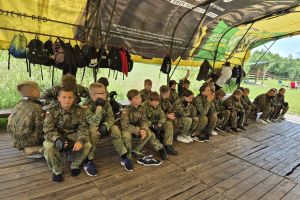 Uczniowie w mundurach czekają na grę w paintball.
