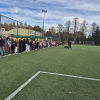 Uczniowie uczestniczą w spotkaniu z policjantami i psem policyjnym.