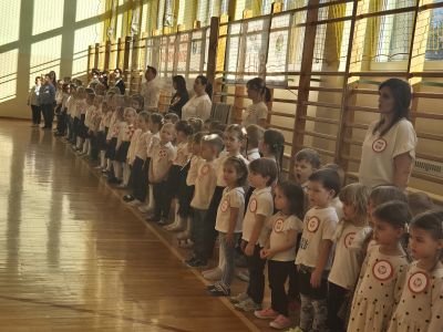 Przedszkolaki na sali gimnastycznej czekają na śpiewanie hymnu.