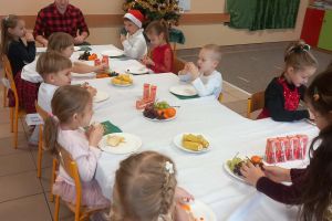 Dzieci na wigilii siedzą za stołami.