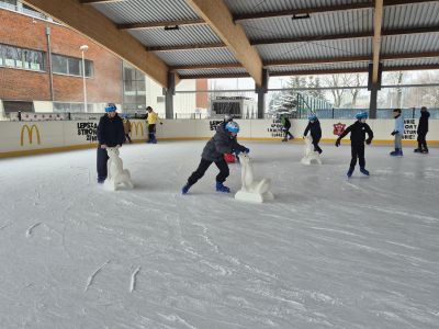 Uczniowie z pingwinkami uczą się jeździć na łyżwach.
