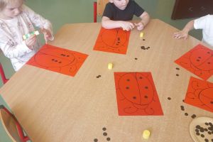 Dzieci przyklejają kropki na sylwety biedronki.