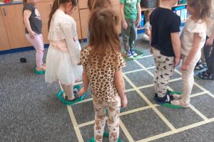 Dzieci uczestniczą w zabawie ruchowej na dywanie.